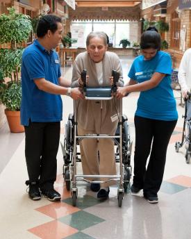 Two team members on either side of a resident, assisting her to walk with a walker